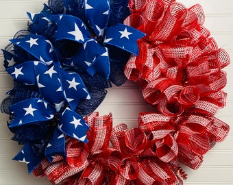May include: A red, white, and blue patriotic wreath made of mesh and ribbon. The wreath is decorated with a blue ribbon with white stars.