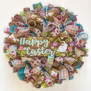 May include: A colorful Easter wreath with a wooden sign that reads "Happy Easter". The wreath is decorated with pink, green, blue, and brown ribbons and mesh. There are also small bunny cutouts on the wreath.