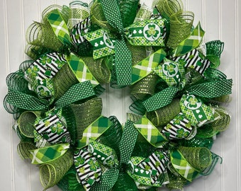 Op de afbeelding: Een groene, witte en zwarte St. Patricks Day krans met klavertjevier en kabouterhoed ontwerpen. De krans is gemaakt van gaas en lint en is versierd met groene glitter.