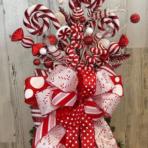 May include: Red and white candy cane Christmas tree topper with a large bow made of red and white polka dot ribbon, striped ribbon, and ribbon with a candy cane pattern.