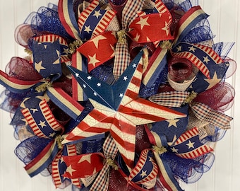 May include: A patriotic wreath decorated with red, white, and blue mesh, ribbons, and a large, distressed metal star. The wreath features a variety of patterns, including stars, stripes, and plaid.