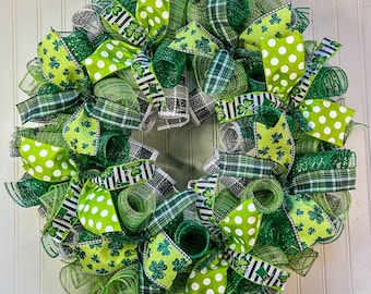 Op de afbeelding: Een groene, witte en zwarte St. Patricks Day krans met klavertje vier en stippenmotief lint. De krans is gemaakt van gaas en heeft verschillende texturen.