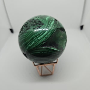 May include: A green malachite sphere on a gold metal stand. The sphere has a swirling pattern of green and black.
