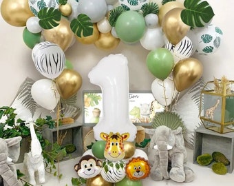 Può includere: Un palloncino bianco con il numero uno con decorazioni di palloncini a forma di giraffa, leone e scimmia. Palloncini verdi, dorati e bianchi sono disposti ad arco. I palloncini sono decorati con stampe di animali della giungla e foglie verdi.