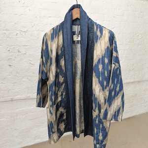 May include: A blue and beige patterned kimono with a denim collar and pockets. The kimono is hanging on a wooden hanger.