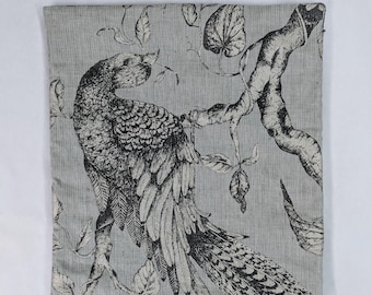 May include: A gray and white throw pillow with a black and white print of a bird perched on a branch with leaves.