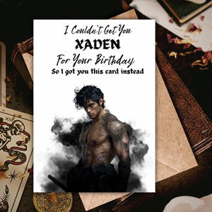 May include: A greeting card with the text "I Couldn't Get You XADEN For Your Birthday So I got you this card instead." The card features an illustration of a shirtless man with tattoos and dark hair. Tarot cards and a book are in the background.