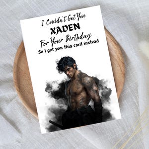 May include: A white greeting card with the text "I Couldn't Get You XADEN For Your Birthday So I got you this card instead." The card features a shirtless man with tattoos, set against a smoky background.