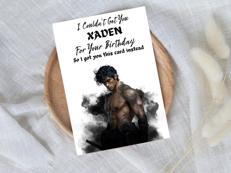 May include: A white greeting card with the text "I Couldn't Get You XADEN For Your Birthday So I got you this card instead." The card features a shirtless man with tattoos, set against a smoky background.