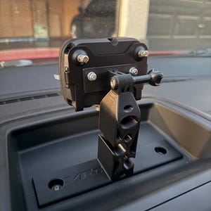 May include: A black camera mount with a GoPro camera attached. The mount is attached to a black dashboard with the word "VRC" printed on it.