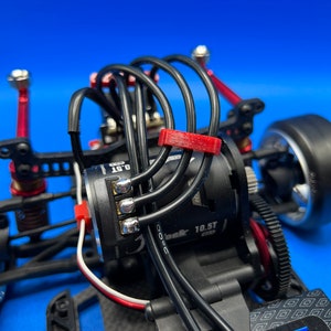 May include: Close-up of a black electric motor with red and white wires. The motor is attached to a black and silver gear. The motor is labeled "10.5T".