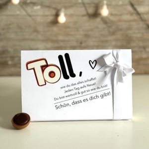 Puede incluir: Una tarjeta blanca con la palabra "Toll" en letras negras y naranjas, un símbolo de corazón y el texto "wie du das alles schaffst! Jeden Tag aufs Neue! Du bist wertvoll & gut so wie du bist! Schön, dass es dich gibt!" en texto negro.