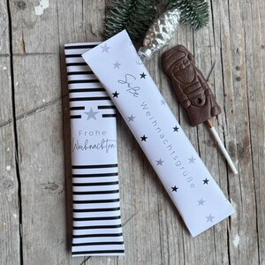 May include: Two white gift bags with black and white stripes and stars. One bag says "Frohe Weihnachten" and the other says "Liebe Weihnachtsgrüße".