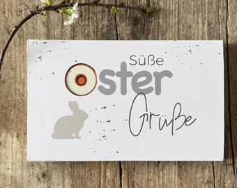 May include: A white card with a gray bunny silhouette, a gray egg with a brown center, and the text "Süße Oster Grüße".