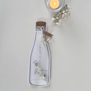 Könnte beinhalten: Eine dekorative Flaschenkarte mit den Wörtern "Post" und "Geburtstags" aufgedruckt. Die Karte hat einen Korken, ist mit Bindfaden und kleinen Blumen gebunden. Eine brennende Kerze in einem Glas und weitere Blumen sind ebenfalls vorhanden.