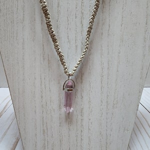 May include: A light pink crystal pendant on a beige macrame cord necklace.