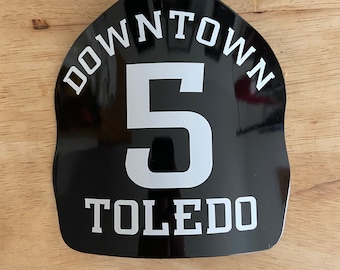 May include: Black firefighter helmet shield with white lettering that reads "DOWNTOWN 5 TOLEDO"