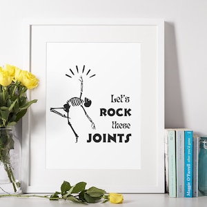 Könnte beinhalten: Ein Schwarzweißdruck eines tanzenden Skeletts mit dem Text "Let's ROCK these JOINTS". Der Druck ist in einem weißen Rahmen gerahmt und wird auf einem weißen Regal mit einer Vase mit gelben Rosen ausgestellt.