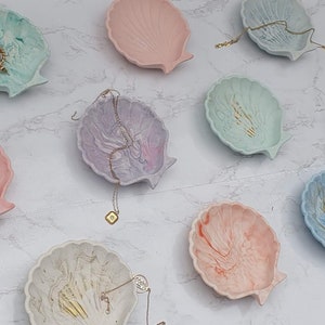 May include: A selection of eight small, decorative, seashell-shaped dishes in a range of pastel colours, including pink, blue, green, and white. Each dish features a unique marbled pattern and gold accents. The dishes are ideal for holding jewellery, rings, or other small items.