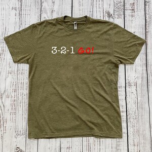 May include: A green t-shirt with the text "3-2-1 GO!" printed in white with the word "GO!" in red.