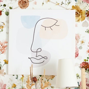 May include: Abstract line art print of a face with closed eyes and a mouth, featuring soft pastel colors in shades of blue, pink, and gray. The print is on a white background.