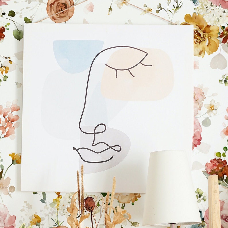 May include: Abstract line art print of a face with closed eyes and a mouth, featuring soft pastel colors in shades of blue, pink, and gray. The print is on a white background.