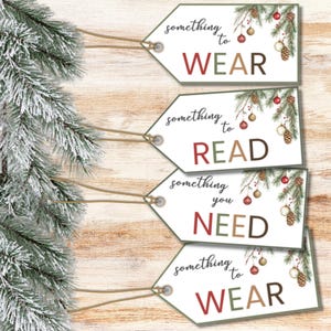 Peut inclure: Quatre étiquettes cadeaux blanches avec le texte : "something to WEAR", "something to READ", "something you NEED", et "something to WEAR". Chaque étiquette présente un motif festif avec des branches de pin, des ornements rouges et dorés, et des pommes de pin.
