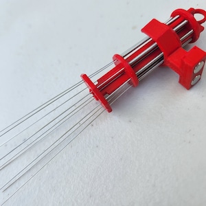 K&ouml;nnte beinhalten: Ein rotes 3D-gedrucktes Werkzeug mit mehreren d&uuml;nnen Metallnadeln, die sich von einem Ende erstrecken. Das Werkzeug hat eine Reihe von Zahnr&auml;dern und einen Griff am anderen Ende.
