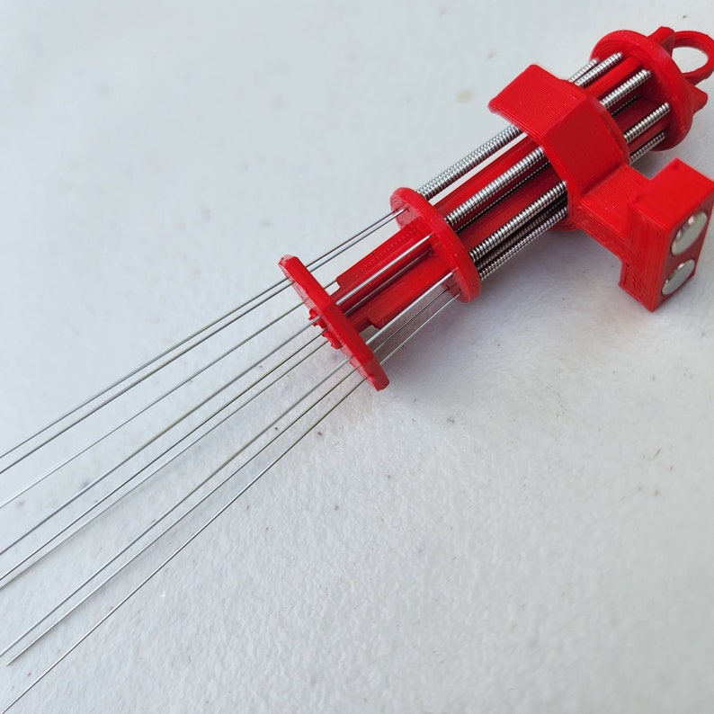 K&ouml;nnte beinhalten: Ein rotes 3D-gedrucktes Werkzeug mit mehreren d&uuml;nnen Metallnadeln, die sich von einem Ende erstrecken. Das Werkzeug hat eine Reihe von Zahnr&auml;dern und einen Griff am anderen Ende.