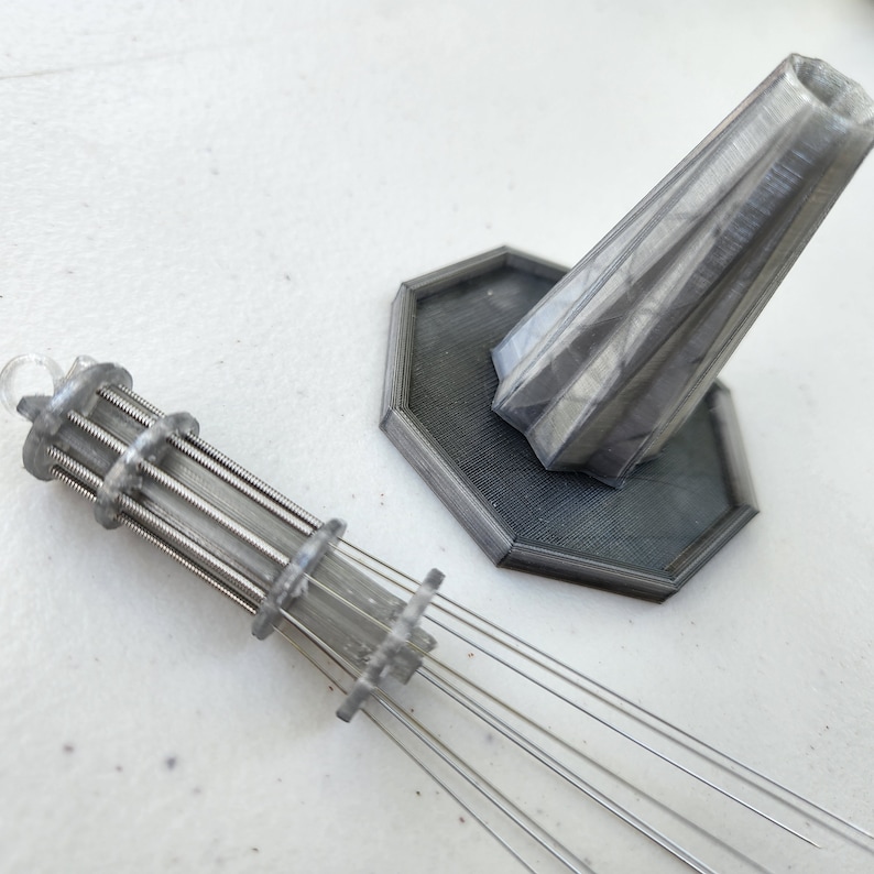 K&ouml;nnte beinhalten: Ein silbernes 3D-gedrucktes Modell eines Turms mit einem Sockel und einer dekorativen Spitze. Der Turm hat eine zylindrische Form mit einer Reihe von Ringen darum herum. Der Sockel ist sechseckig mit einer strukturierten Oberfl&auml;che. Die Spitze ist kegelf&ouml;rmig mit einer spitzen Spitze.