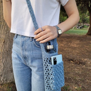 May include: A light blue crocheted bag with a water bottle and a phone inside. The bag is worn over the shoulder as a crossbody bag.