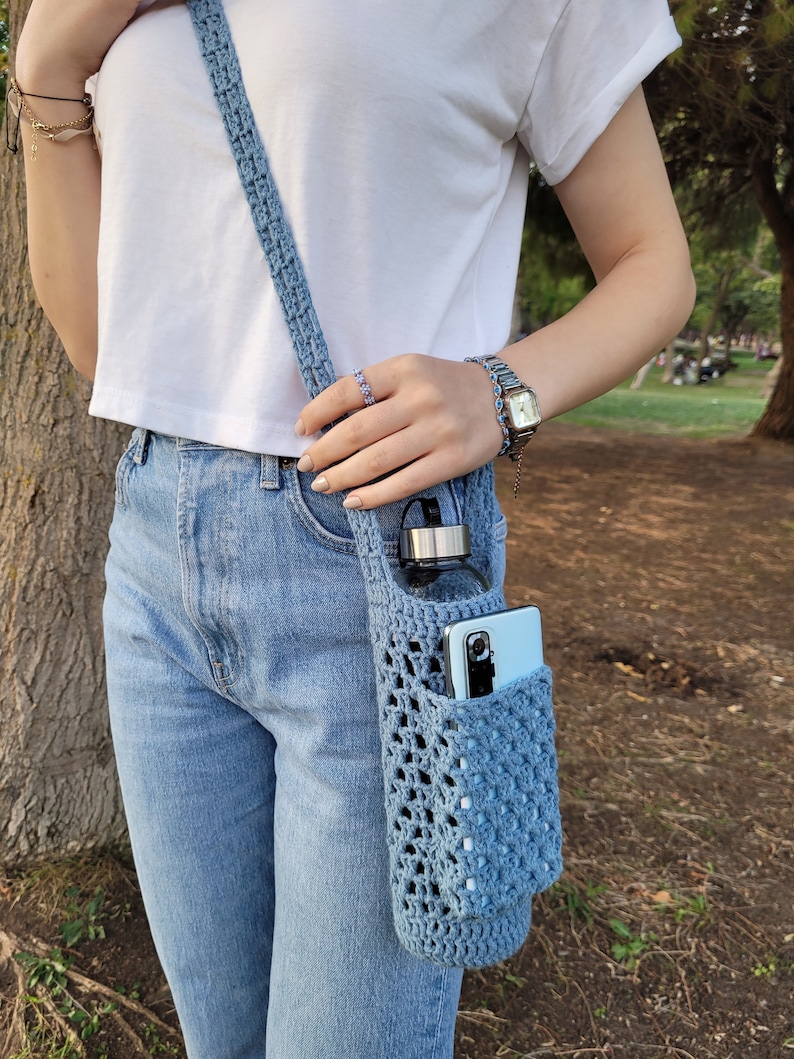 May include: A light blue crocheted bag with a water bottle and a phone inside. The bag is worn over the shoulder as a crossbody bag.