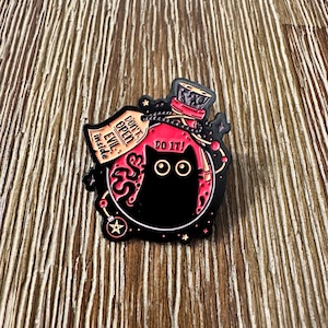 Może przedstawiać: Czarny emaliowany pin przedstawiający czarnego kota w czerwonej butelce z eliksirem. Butelka ma korek, a na butelce widnieje napis "DO IT!". Mała etykieta głosi "DON'T OPEN EVIL INSIDE".