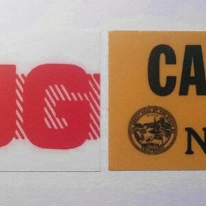 May include: Two rectangular stickers. One white sticker with the red word "AUG" over a striped background. The other is a yellow sticker with "CA 86" in black, a circular emblem, and the numbers "N 52654".