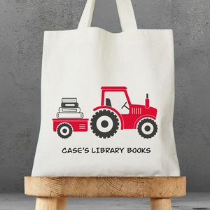 May include: A white canvas tote bag with a red tractor pulling a wagon full of books. The text "CASE'S LIBRARY BOOKS" is printed on the bag.