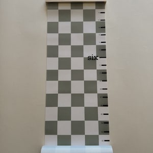 May include: A white and gray checkered growth chart with a wooden top rail and a black string. The chart has black markings with numbers from 62 to 78 inches. The word "six" is printed in black on the chart.