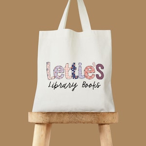 May include: White tote bag with a colorful patchwork design that reads "Lettie's Library Books".