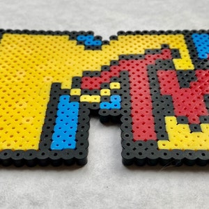 May include: A pixel art rendition of the MTV logo, made with colorful beads. The logo is yellow, red, blue, and black.