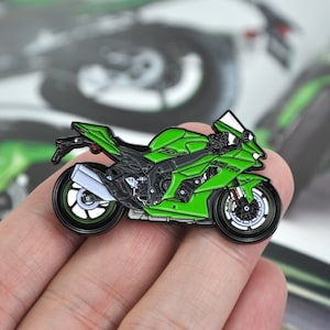 Puede incluir: Pin de motocicleta verde y negra con un diseño detallado. El pin presenta una moto deportiva con un tubo de escape blanco y ruedas negras. La motocicleta está sobre un fondo borroso.