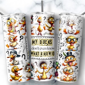 May include: A white cylindrical tumbler with a metal straw featuring a repeating pattern of cartoon ducks with various expressions and accessories, interspersed with question marks and scribbles, and the text MY DUCKS don't even know WHAT A ROW IS.
