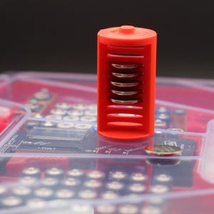 May include: A red plastic battery holder with a clear plastic case. The holder has six slots for batteries and the text "Battery Daddy" is printed on the case.