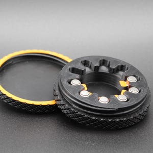 May include: A black plastic ring with a yellow inner rim and a series of small metal balls set into the outer edge. The ring has a textured surface.