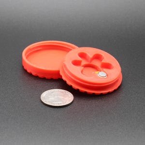 May include: A red plastic container with a paw print design on the lid. The container is open and a small silver coin is visible inside.