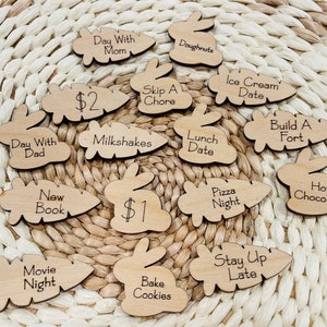 May include: Wooden tokens with various activities and prices written on them. The tokens are shaped like carrots and bunnies. Some of the activities include: Day with Mom, Day with Dad, Skip a Chore, Ice Cream Date, Lunch Date, Build a Fort, Pizza Night, Hot Chocolate, New Book, Movie Night, Milkshakes, Bake Cookies, Stay Up Late, Doughnuts, $1, $2.
