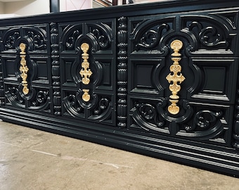 May include: A black dresser with ornate carvings and gold-colored hardware. The dresser has multiple drawers and a detailed, vintage design. The gold hardware provides a striking contrast against the dark finish, adding a touch of elegance.