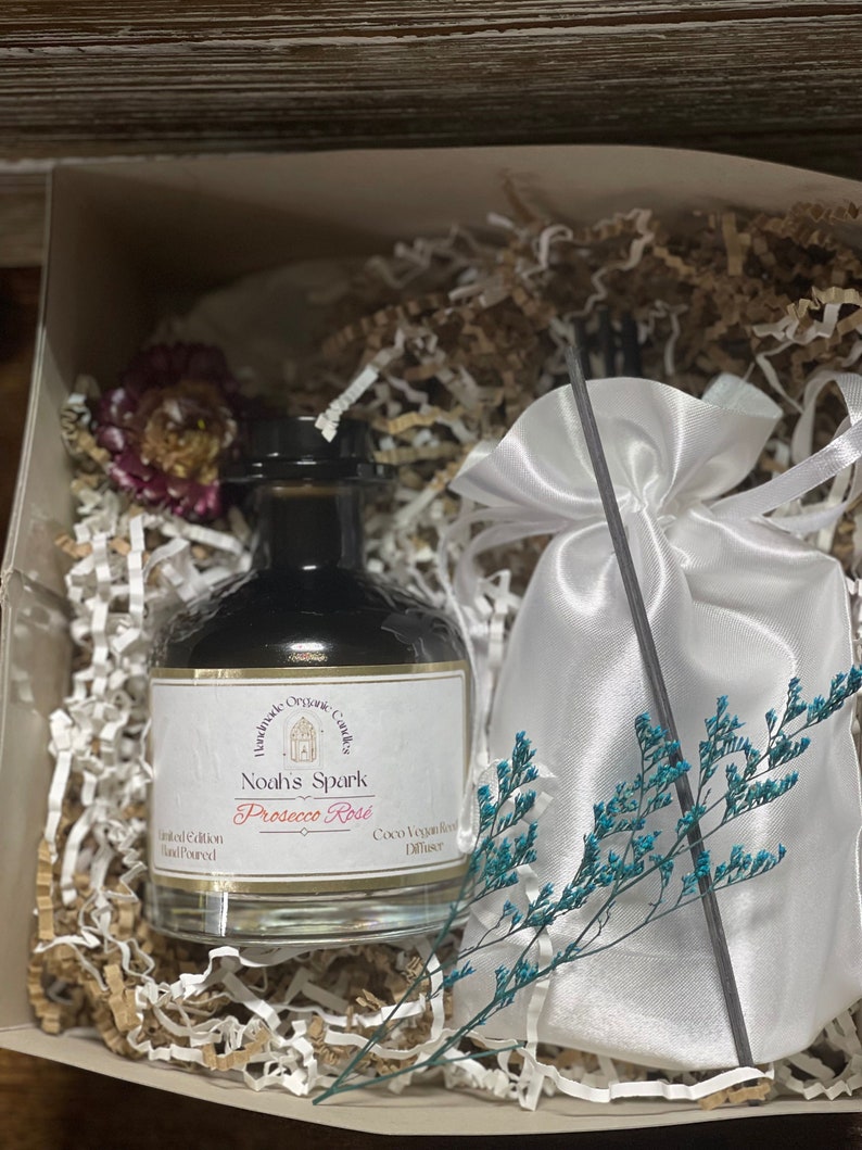 May include: A glass bottle of  'Noah's Spark Prosecco Rose'  coco vegan reed diffuser, hand-poured in a white gift box with shredded paper and a white satin bag with a black reed diffuser stick.