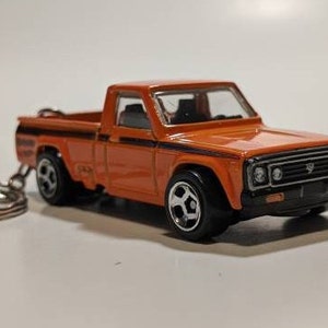 May include: Orange toy truck with a black stripe and a silver keyring attached. The truck has a black front bumper and black wheels.