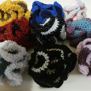 May include: Eight crocheted flower-shaped hair scrunchies in various colors, including gray, black, pink, purple, blue, and red.