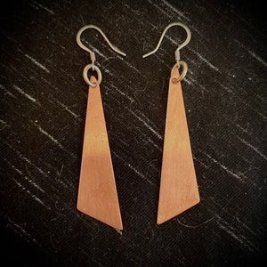May include: A pair of copper triangle earrings with silver hooks. The earrings are a light copper color with a subtle sheen.