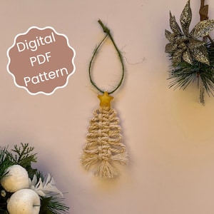 May include: A white and gold macrame Christmas tree ornament with a yellow star on top. The ornament is hanging from a green string. The text "Digital PDF Pattern" is visible in the image.